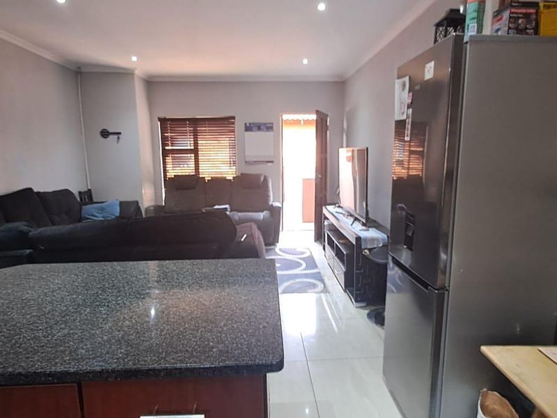Open-plan living area featuring a kitchen with granite countertops and tiled flooring, flowing into a comfortable lounge space with direct outdoor access.
