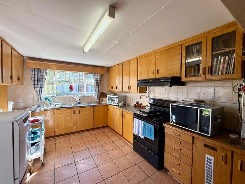 A functional kitchen featuring traditional wooden cabinetry, tiled backsplash, and tiled flooring, offering a classic layout with ample storage and workspace.