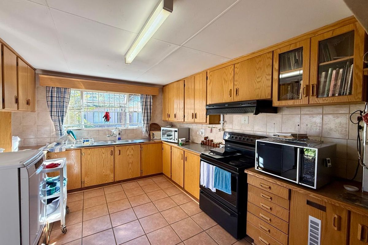 A functional kitchen featuring traditional wooden cabinetry, tiled backsplash, and tiled flooring, offering a classic layout with ample storage and workspace.