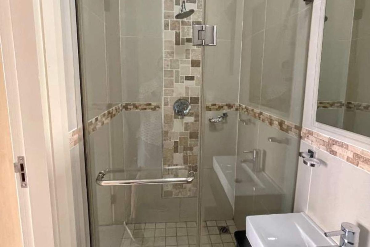 A modern bathroom featuring a glass-enclosed shower with decorative mosaic tile accents, a vanity basin, and neutral wall tiling.