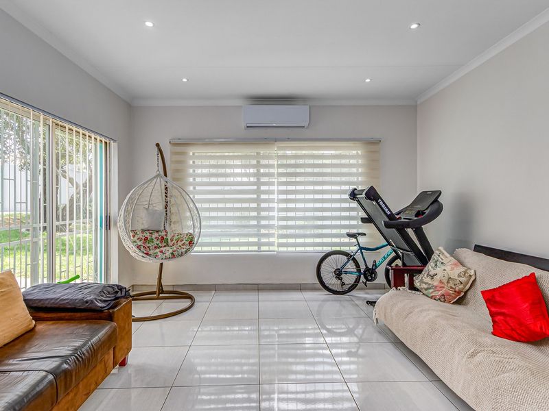 A bright living room featuring white tiled flooring, recessed ceiling lights, a wall-mounted air conditioning unit, and large sliding doors leading to the garden.