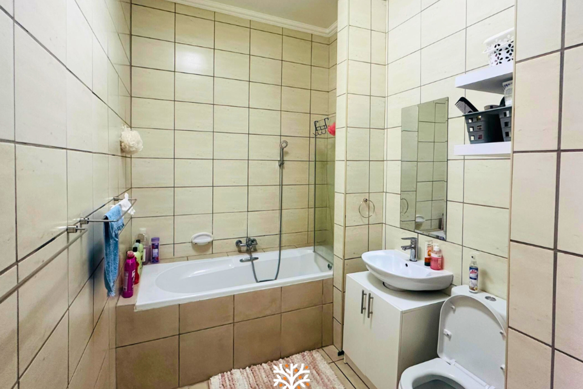 A functional bathroom featuring a built-in bathtub with shower attachment, a pedestal-style vanity basin, and a standard toilet, finished with full-height wall tiling.