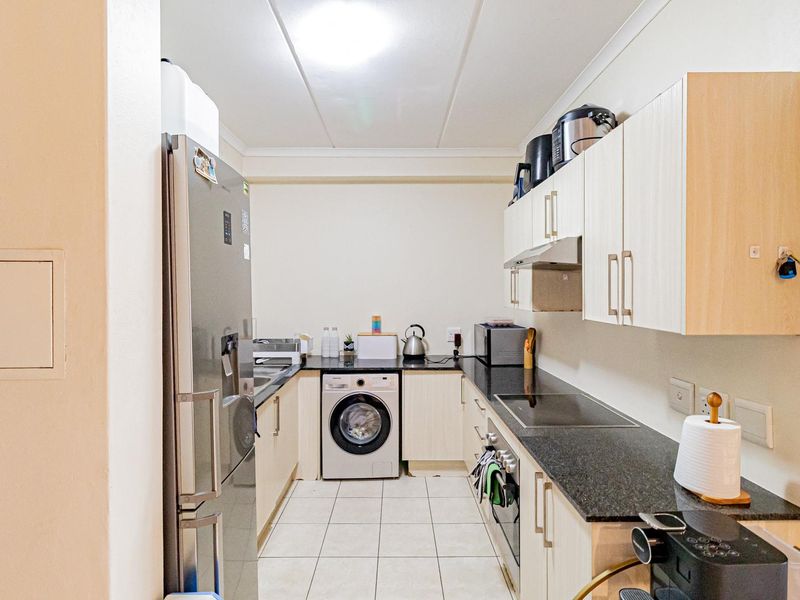 Compact galley-style kitchen featuring light wood-finish cabinetry, dark granite countertops, integrated oven, electric hob, and tiled flooring.