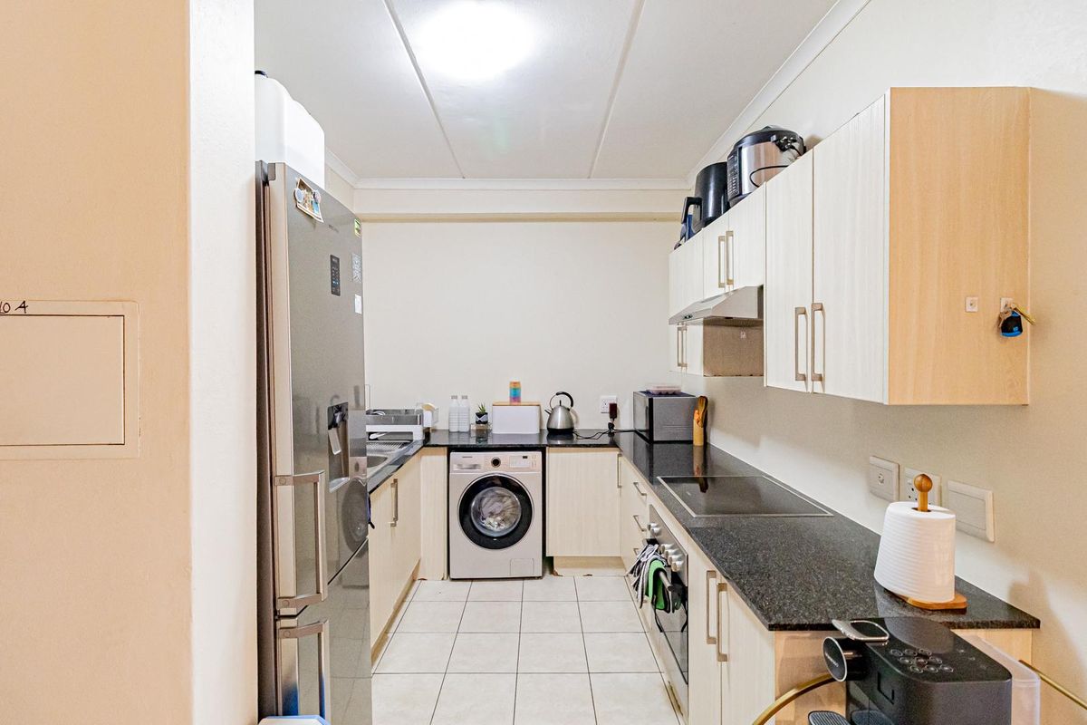 Compact galley-style kitchen featuring light wood-finish cabinetry, dark granite countertops, integrated oven, electric hob, and tiled flooring.