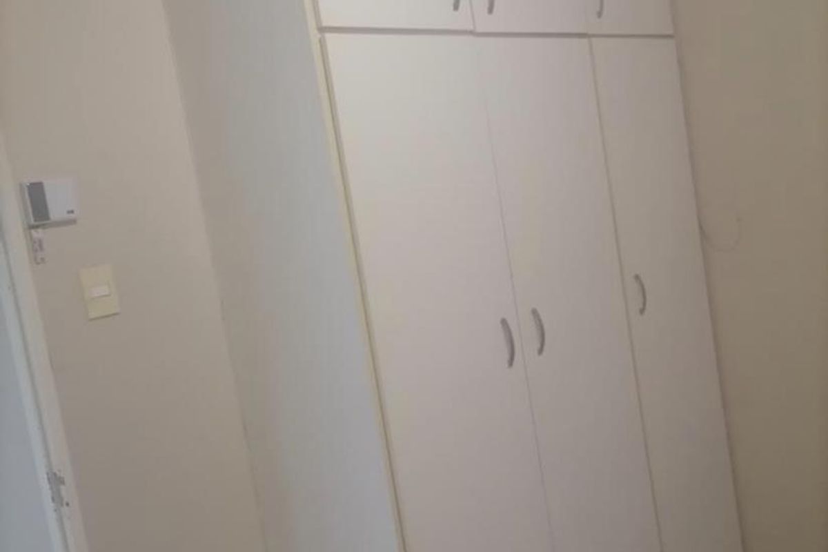 A bedroom featuring white built-in cupboards with overhead storage and tiled flooring.