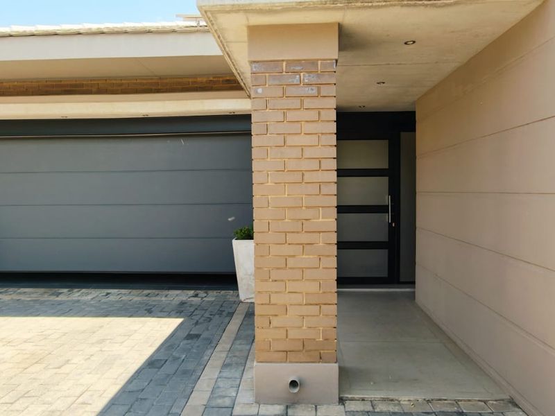 Modern front facade featuring a paved driveway, automated garage door, and a covered entrance with a contemporary front door.