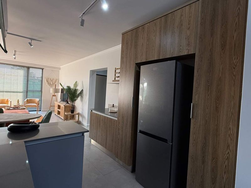 Modern open-plan living area featuring a contemporary kitchen with wood-finish cabinetry, stone countertops, and seamless flow to the lounge with large sliding glass doors.
