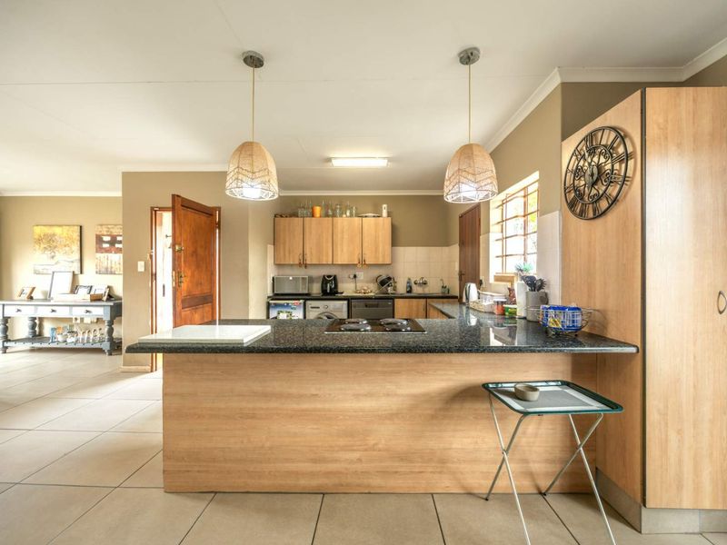 Open plan kitchen featuring granite countertops, light wood cabinetry, and pendant lighting, seamlessly flowing into the adjacent living area with tiled flooring throughout.