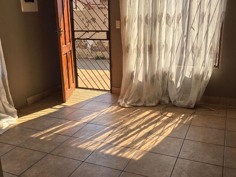 An empty living room featuring tiled flooring, a security gate at the entrance, and natural light streaming through the window.