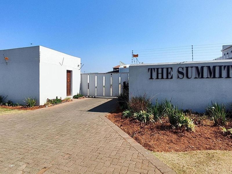 The entrance to The Summit apartment complex, featuring a paved driveway, secure gate access, and perimeter electric fencing.
