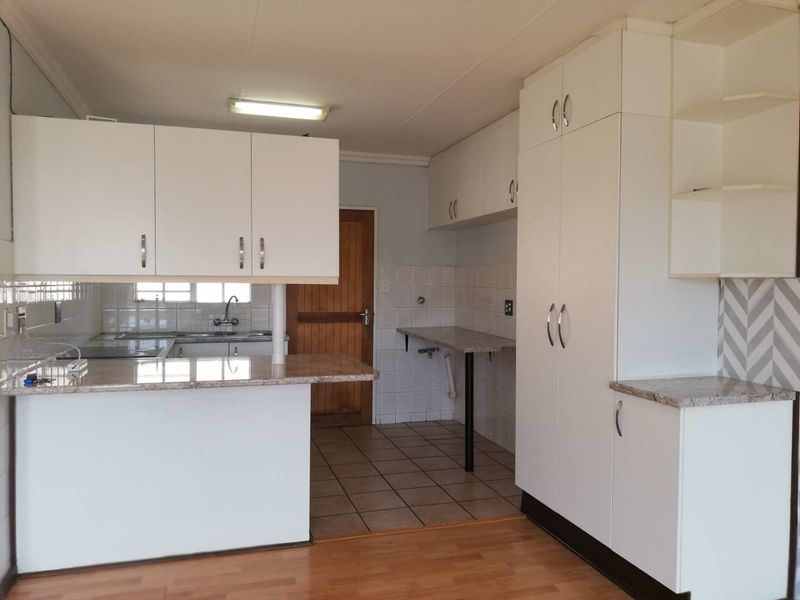A functional kitchen featuring white cabinetry, granite countertops, tiled backsplash, and a combination of ceramic tile and laminate flooring.