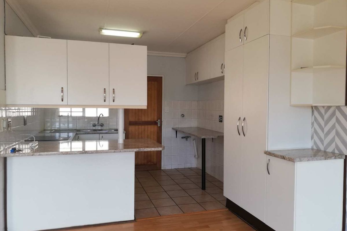 A functional kitchen featuring white cabinetry, granite countertops, tiled backsplash, and a combination of ceramic tile and laminate flooring.