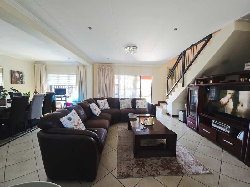 Spacious open-plan living and dining area featuring tiled flooring, a staircase with a metal balustrade, and sliding doors leading to the outdoor space.