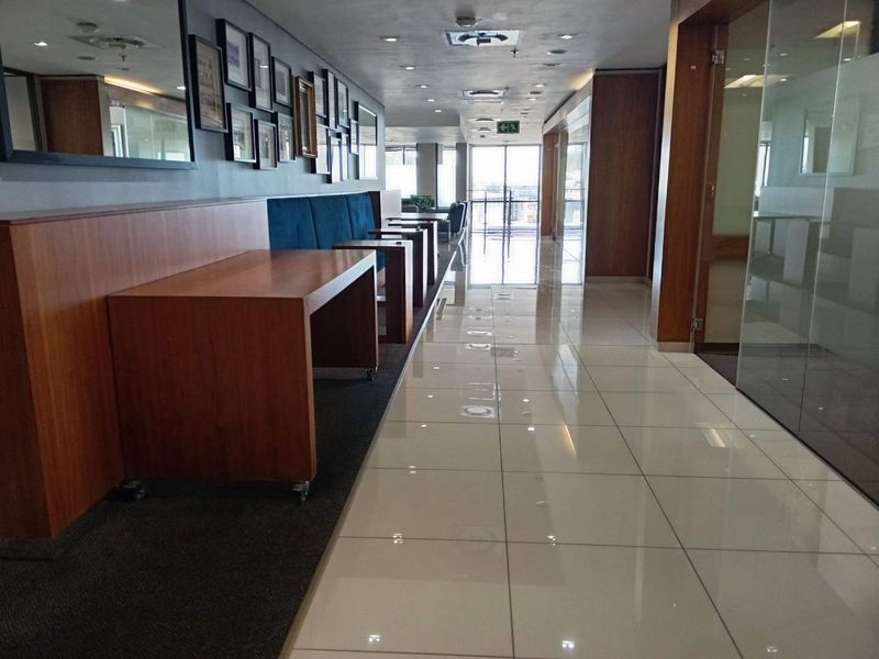 Modern office corridor featuring polished tile flooring, glass partitions, and integrated wooden cabinetry, providing a professional and well-maintained workspace environment.
