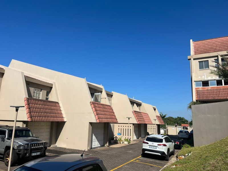 Front elevation of a multi-unit apartment complex featuring paved driveway access, individual garage doors, and tiled roof accents under a clear sky.