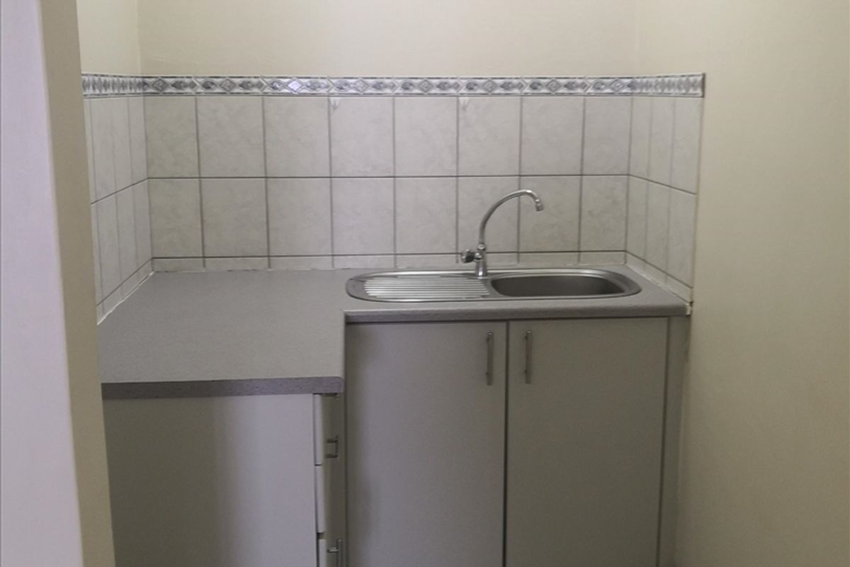A compact kitchenette area featuring built-in cabinetry, a stainless steel sink with faucet, and tiled splashback.