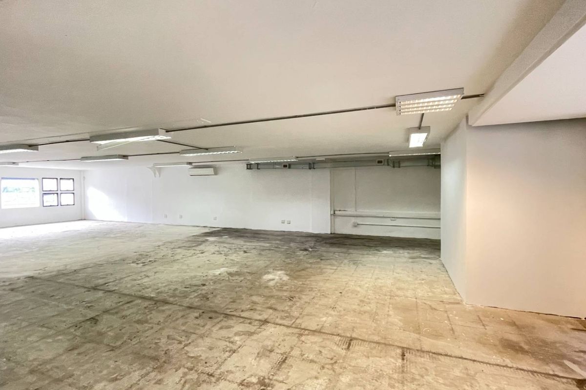 A large, vacant open-plan retail space featuring exposed conduit, fluorescent lighting, air conditioning, and worn concrete flooring ready for renovation.