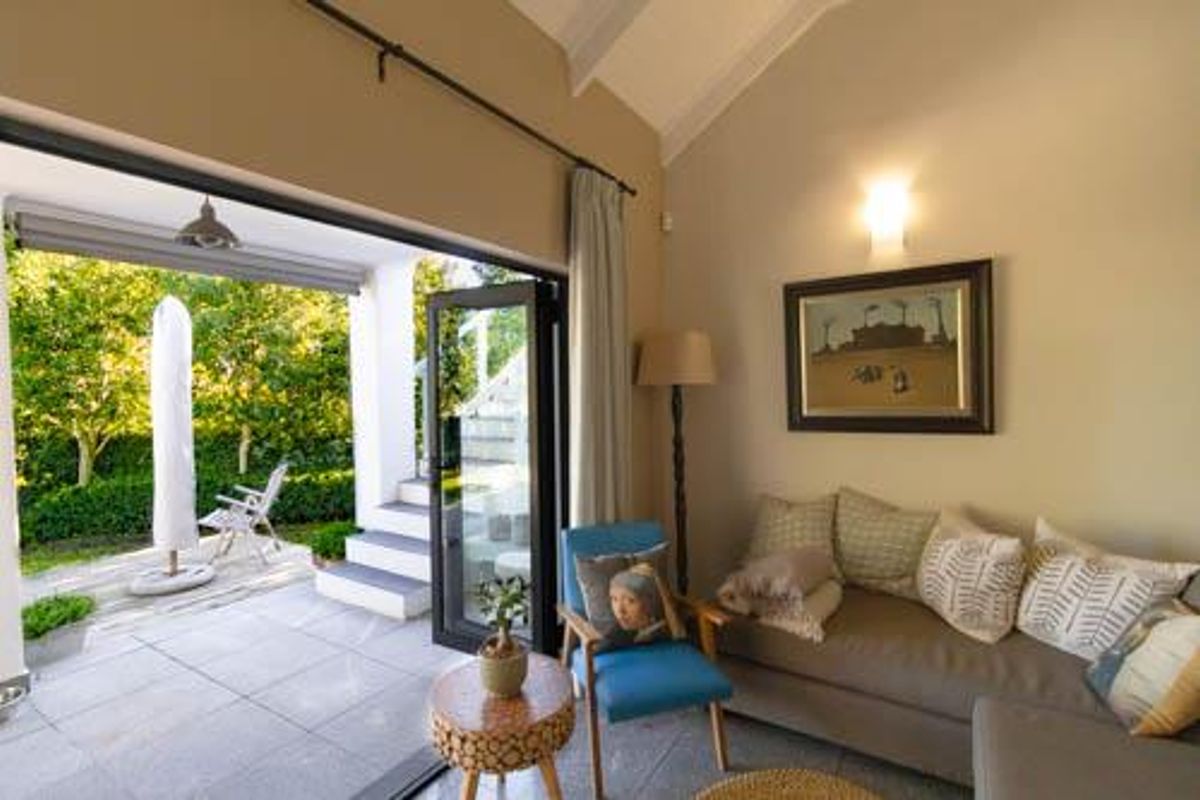 A bright living room featuring a vaulted ceiling and large bi-fold doors that open onto a paved patio area.