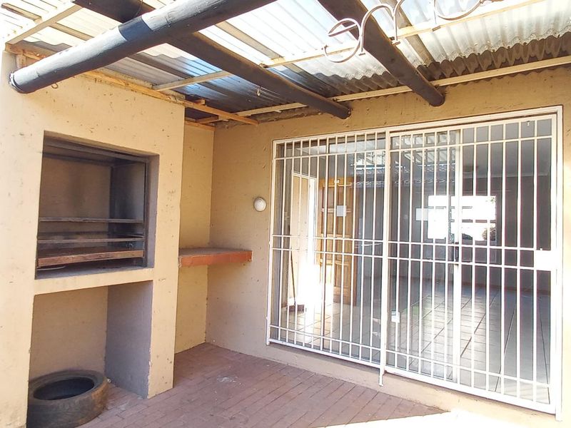 Covered outdoor patio area featuring a built-in braai, paved flooring, and direct access to the interior through a security gate.