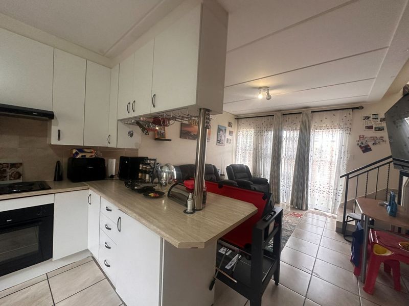 Open-plan kitchen and living area featuring white cabinetry, tiled flooring, and a breakfast bar, leading towards a bright lounge space with staircase access.