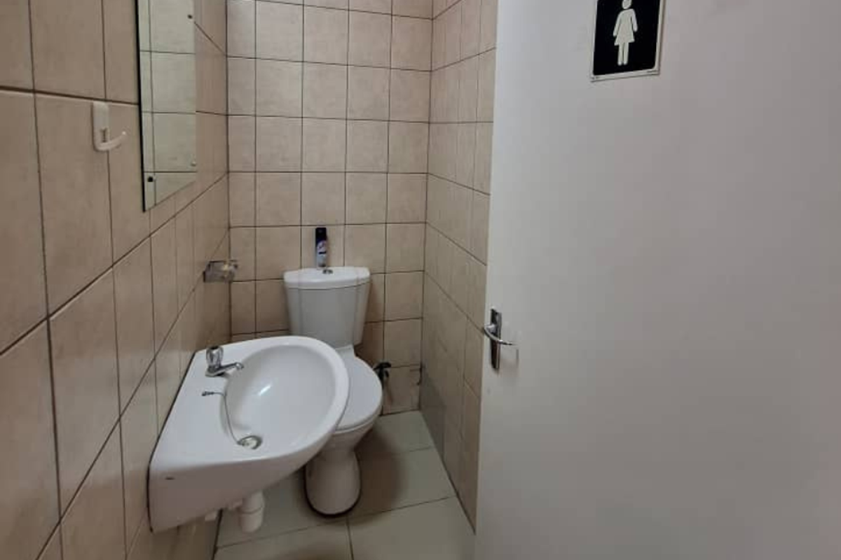 A functional office restroom featuring a wall-mounted basin, toilet, and neutral ceramic tiling throughout.