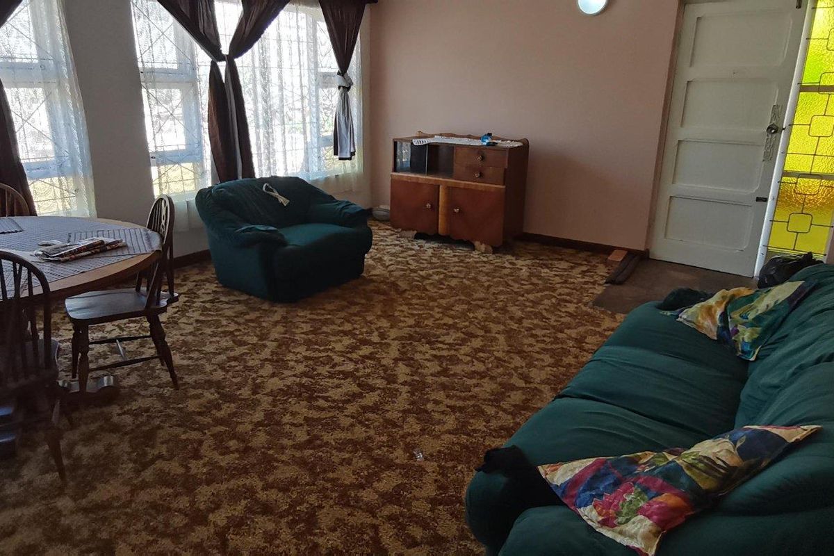 A spacious living and dining area featuring large windows, patterned carpet flooring, and a classic interior layout.