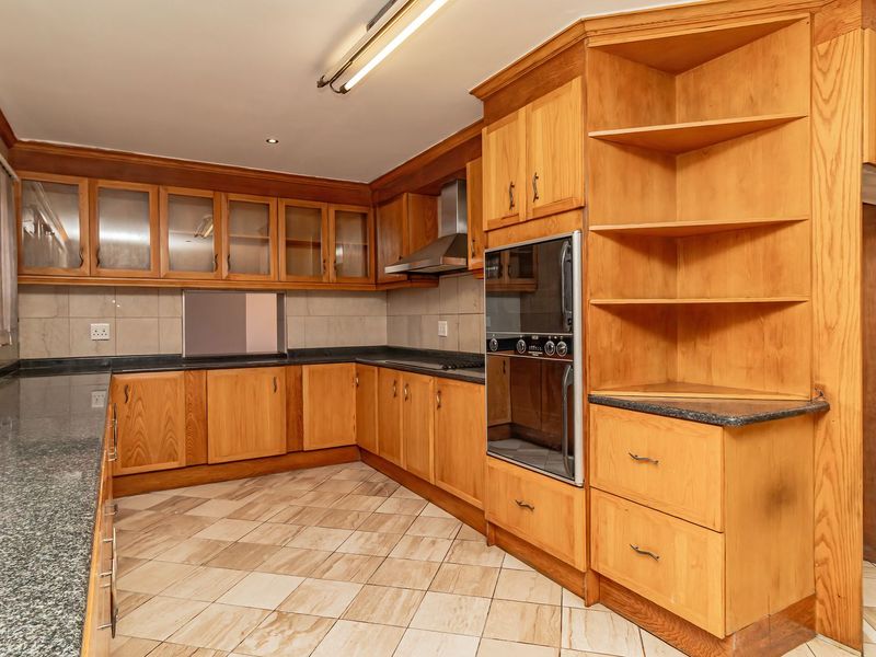 Spacious kitchen featuring extensive wooden cabinetry, granite countertops, built-in double oven, stainless steel extractor fan, and neutral tiled flooring.