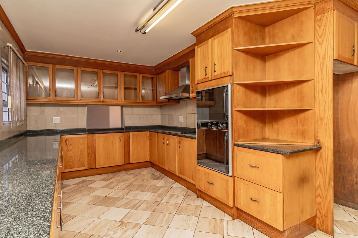 Spacious kitchen featuring extensive wooden cabinetry, granite countertops, built-in double oven, stainless steel extractor fan, and neutral tiled flooring.