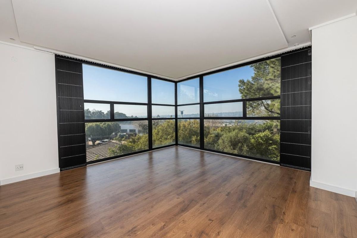 Bright and spacious living area featuring expansive corner windows with panoramic views and modern wood-look flooring.