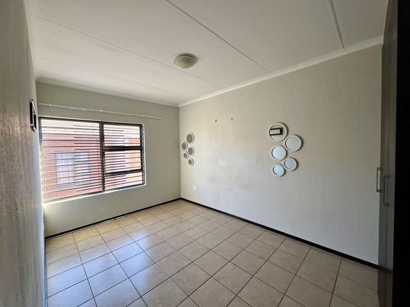 A vacant bedroom featuring tiled flooring, a built-in cupboard, and an aluminium window frame, offering a neutral canvas for personalization.