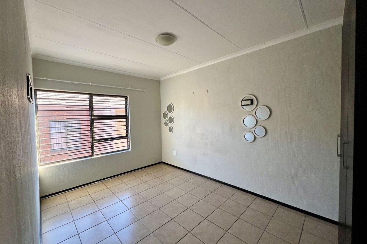 A vacant bedroom featuring tiled flooring, a built-in cupboard, and an aluminium window frame, offering a neutral canvas for personalization.