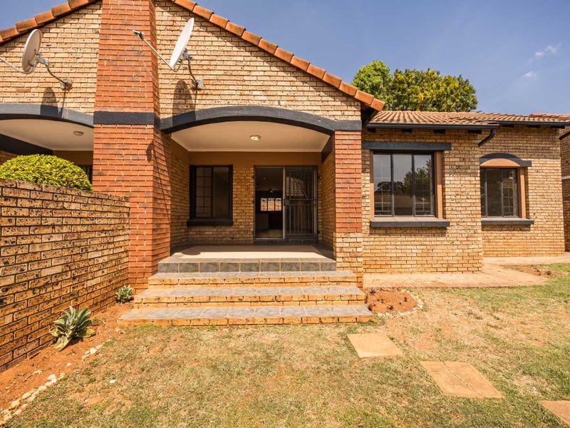 Rear view of a brick townhouse featuring a covered patio, tiled roof, and a private garden area with a brick boundary wall.