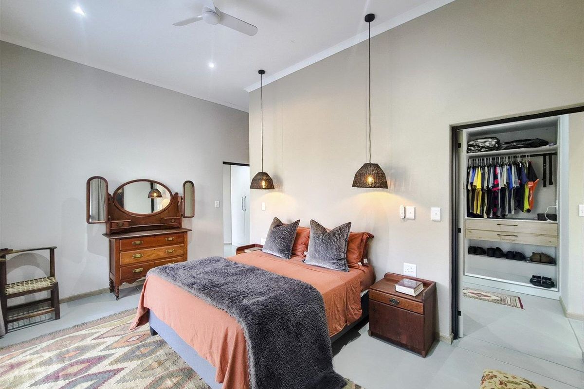 Spacious bedroom featuring polished concrete floors, recessed downlighting, a ceiling fan, and a walk-in wardrobe with built-in shelving.