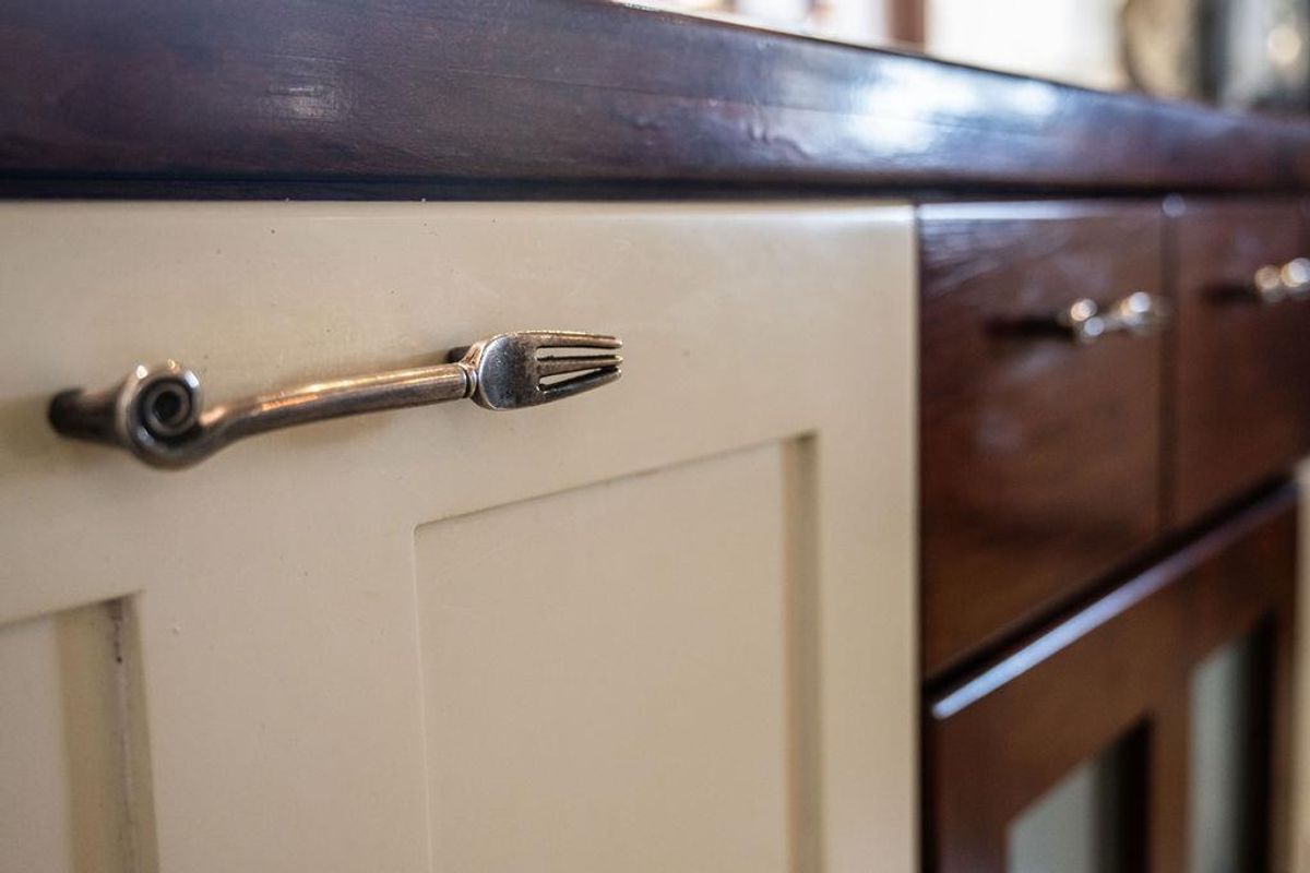 Close-up view of kitchen cabinetry featuring two-tone cream and dark wood finishes with unique decorative metal hardware.