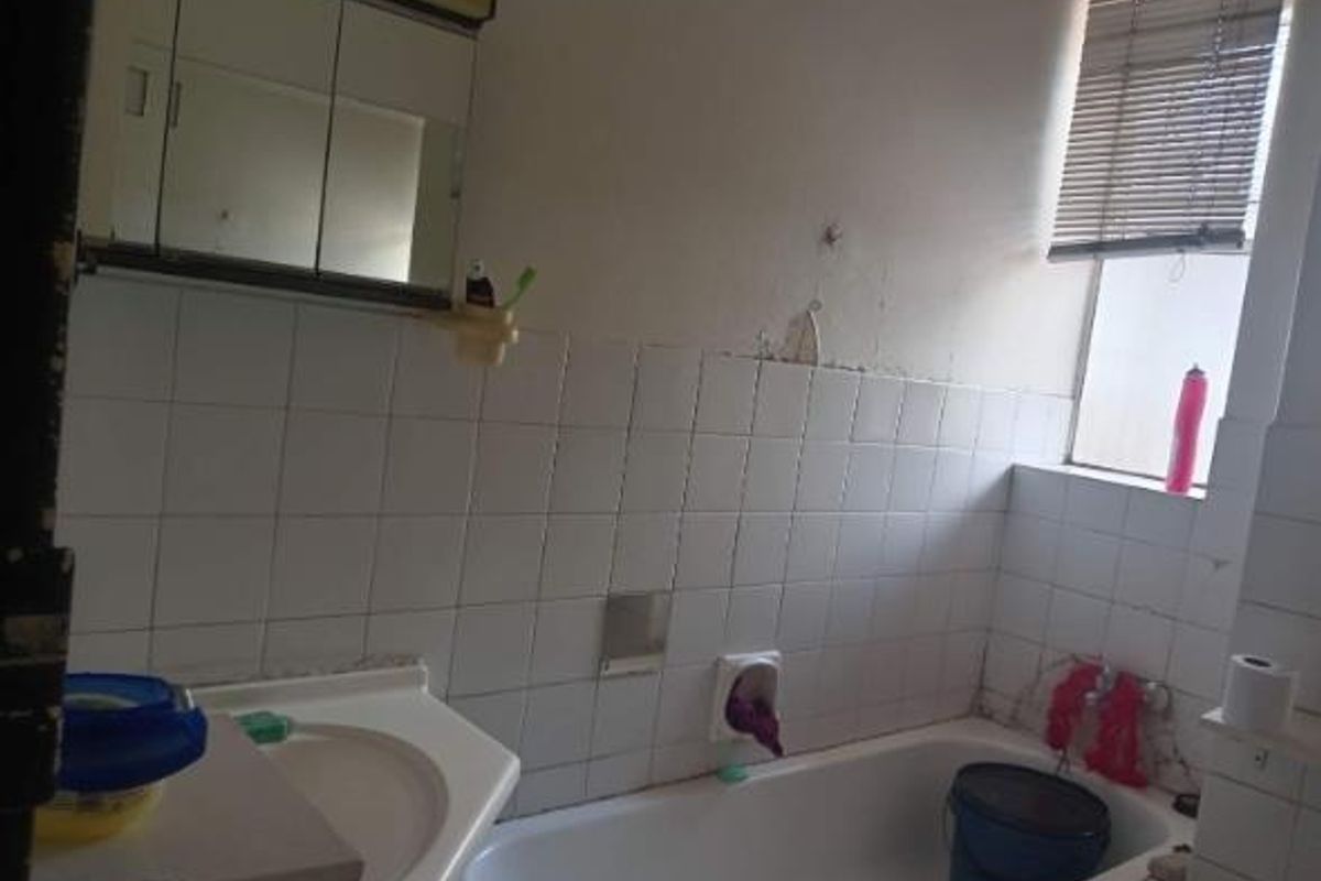 A dated bathroom featuring a standard bathtub, vanity basin, and mirrored medicine cabinet, requiring cosmetic updates and wall repairs.