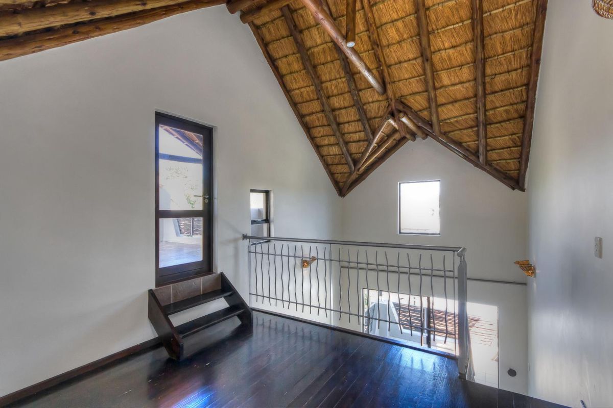 A mezzanine level featuring a high vaulted thatched ceiling, dark timber flooring, and a decorative metal balustrade overlooking the lower level.