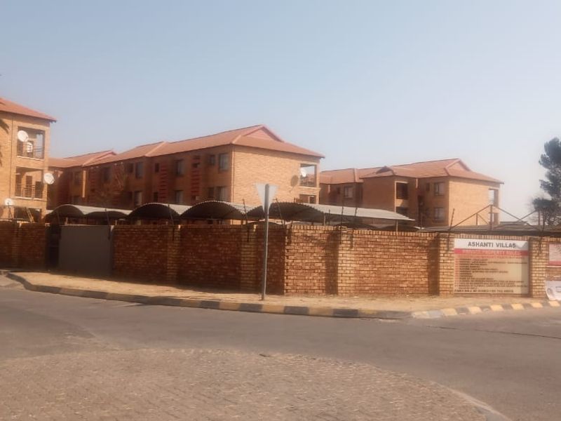 Exterior view of Ashanti Villas apartment complex featuring brick facade buildings, secure perimeter walling, and gated access from the street.
