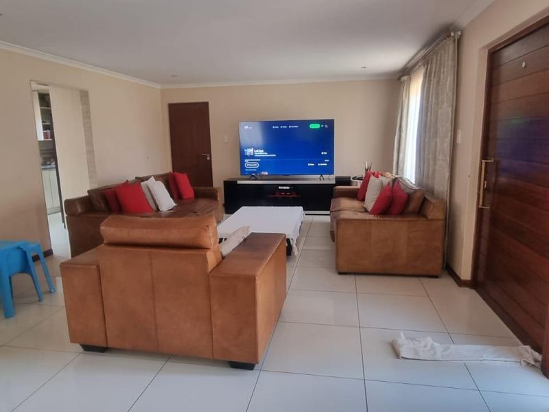 Spacious living room featuring large format floor tiles, recessed downlighting, and a solid timber entrance door, creating a bright and functional open-plan living space.