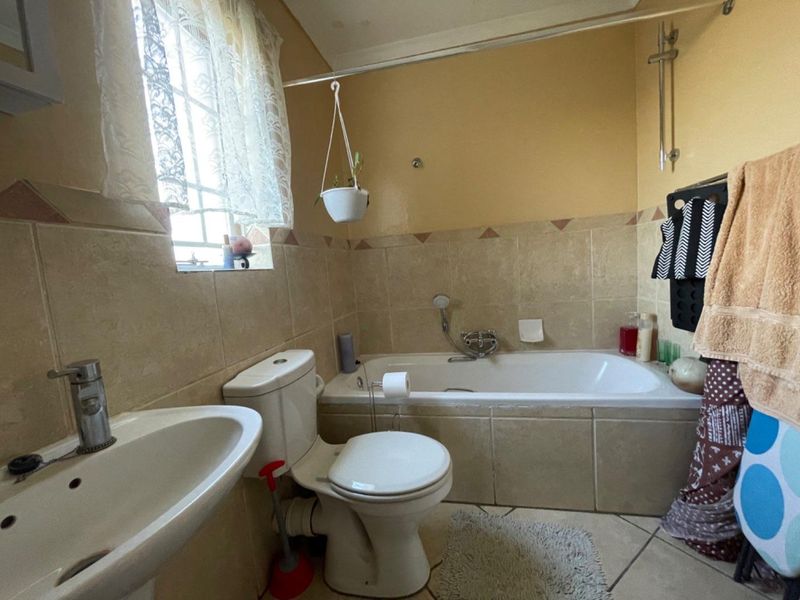 A functional bathroom featuring a bathtub with shower attachment, pedestal basin, and toilet, finished with neutral wall and floor tiling.