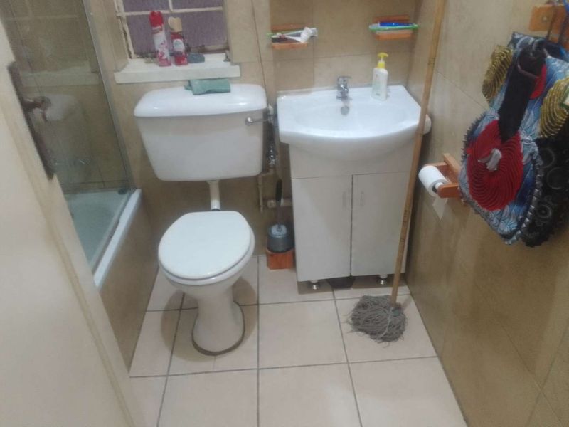 Compact bathroom featuring a toilet, vanity basin, and a shower enclosure with tiled finishes throughout.