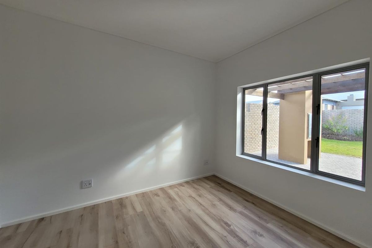 A bright, empty bedroom featuring modern wood-look flooring, neutral walls, and a large window overlooking the rear garden and patio area.