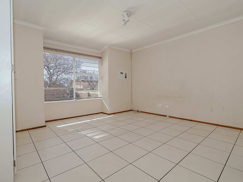 A vacant bedroom featuring tiled flooring, a built-in cupboard, and a large window with blinds, offering a neutral canvas for personalization.