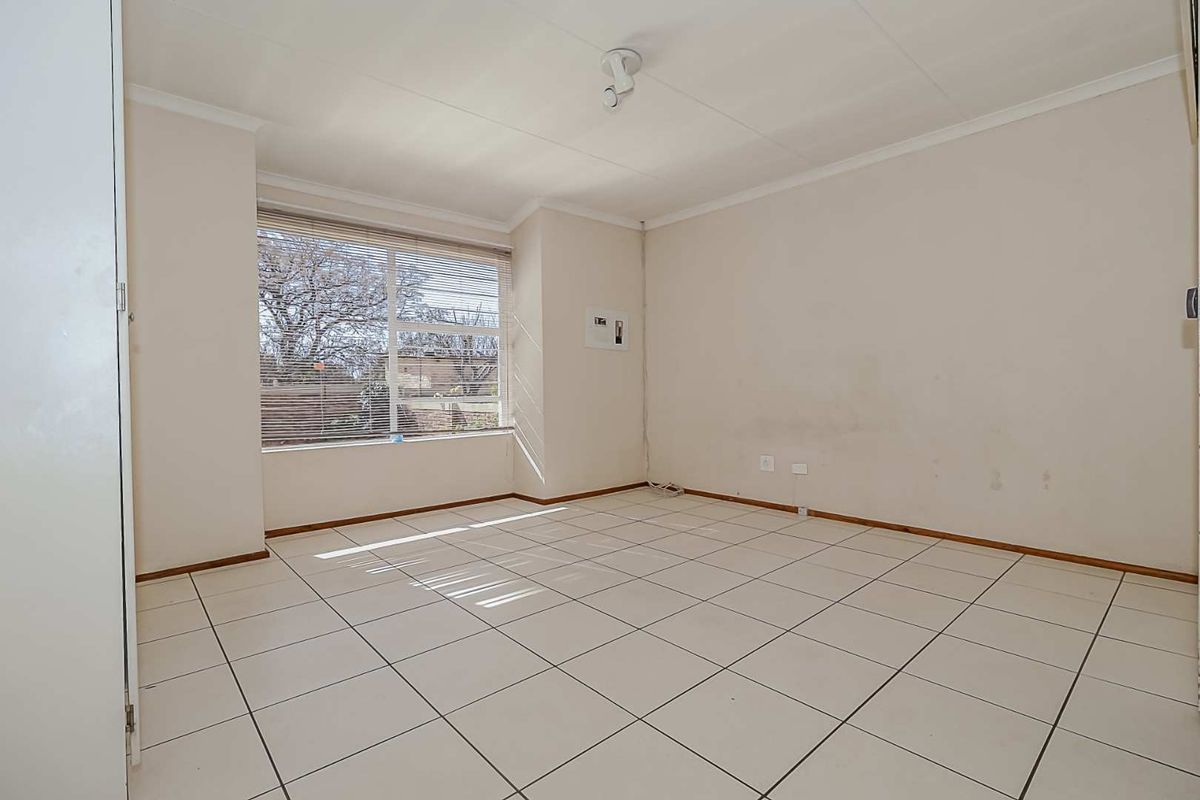 A vacant bedroom featuring tiled flooring, a built-in cupboard, and a large window with blinds, offering a neutral canvas for personalization.