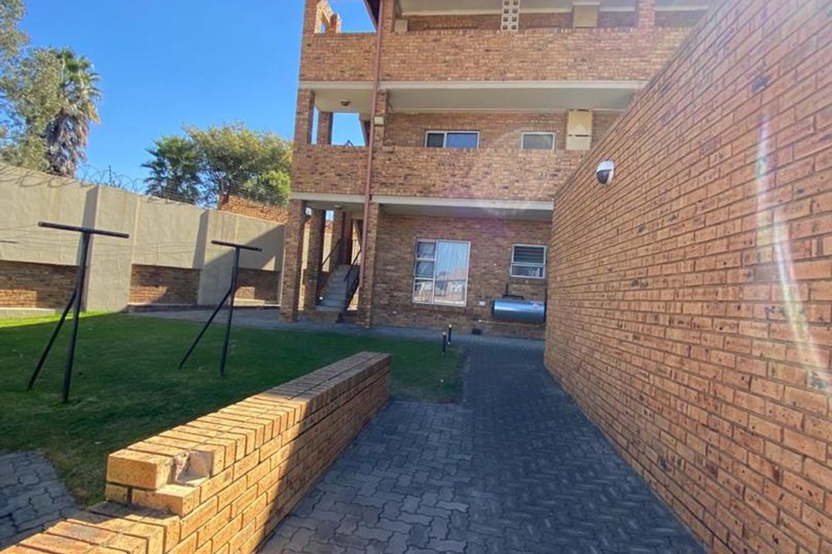 Rear view of a multi-story brick townhouse complex featuring a paved walkway, retaining wall, and shared garden space.
