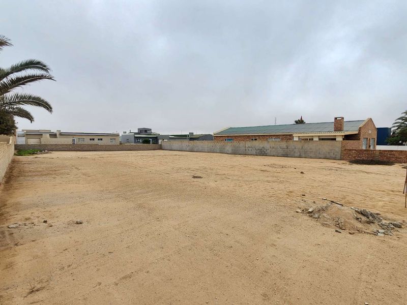 A vacant residential plot featuring a sandy surface and enclosed by perimeter boundary walls, offering a clear space for future development.