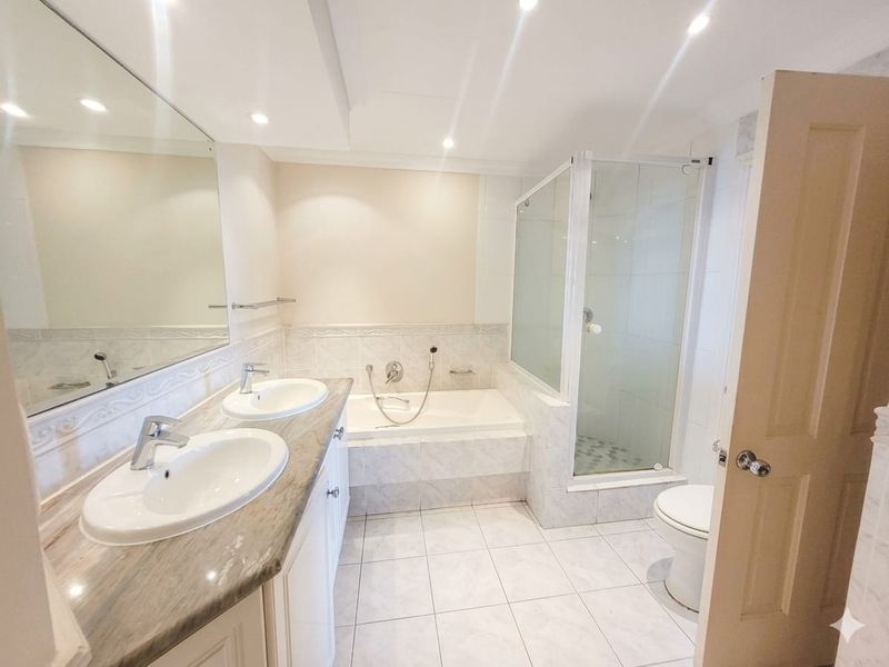 A spacious, well-lit bathroom featuring a double vanity, a built-in bathtub, and a separate glass-enclosed shower with neutral tiled finishes.