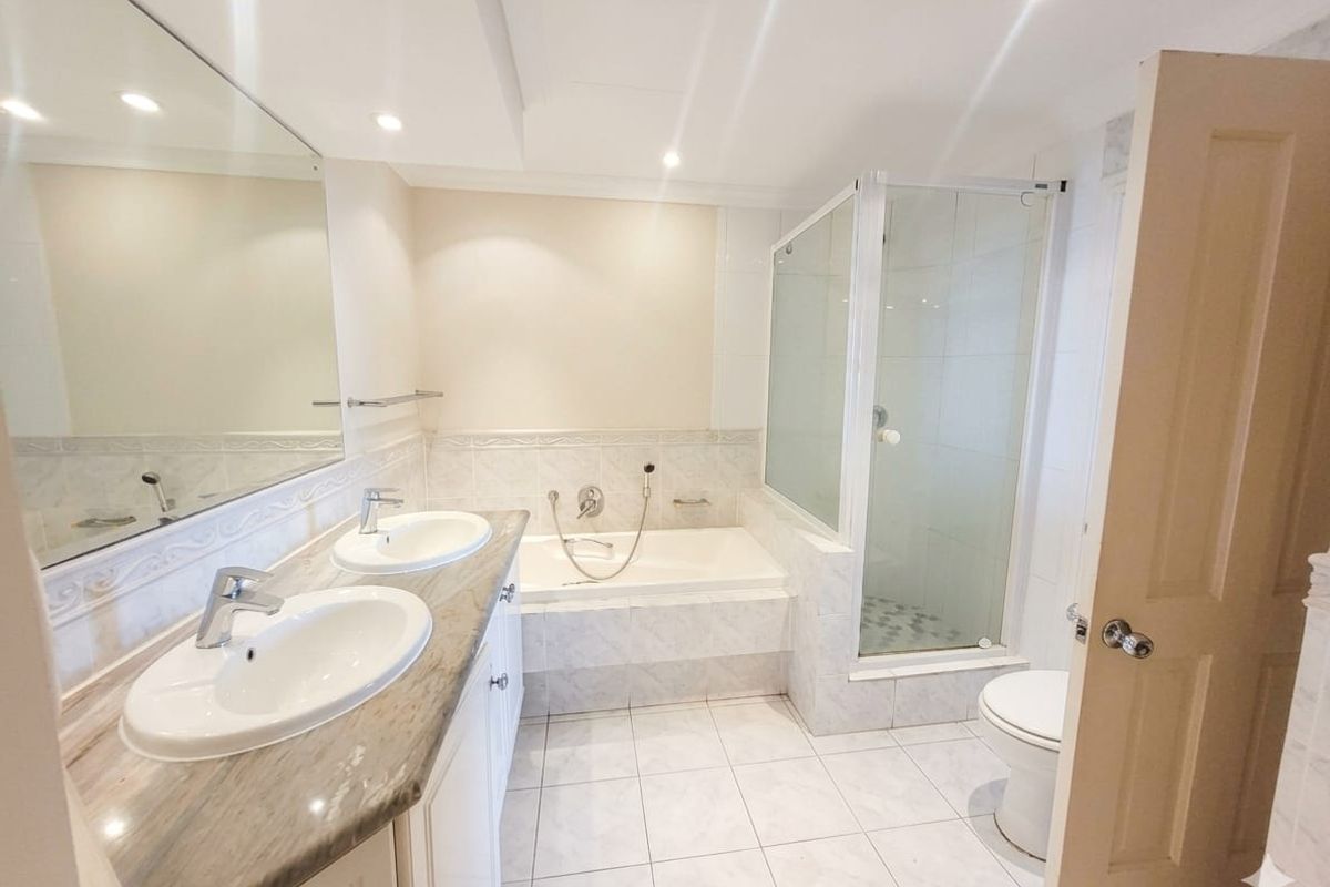 A spacious, well-lit bathroom featuring a double vanity, a built-in bathtub, and a separate glass-enclosed shower with neutral tiled finishes.