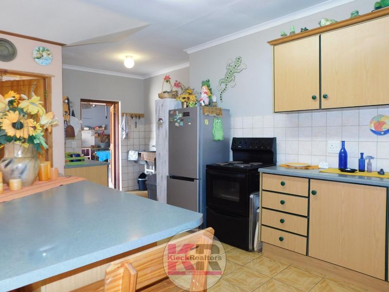 A functional kitchen featuring laminate cabinetry, tiled backsplash, and a freestanding oven, with an adjacent scullery area visible through the doorway.