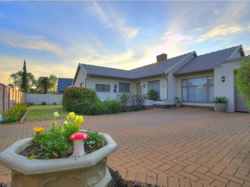 Front view of a residential property featuring a paved driveway, landscaped garden, and secure boundary wall with electric fencing.