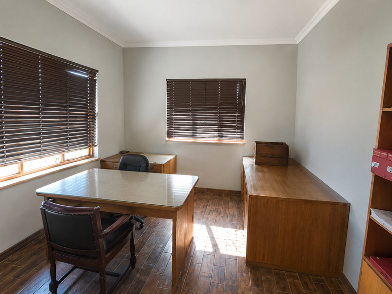 A well-maintained office space featuring timber-look flooring, crown molding, and dual windows fitted with venetian blinds, providing a professional and functional work environment.